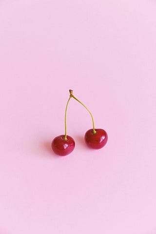 Two ripe cherries on a pink splashback