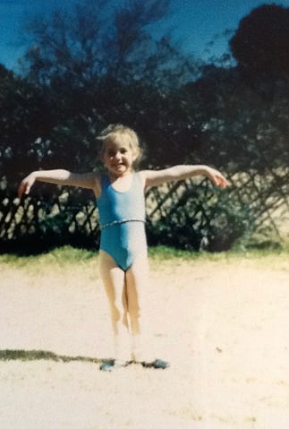 young girl in a blue leotard standing in ballet first position with arms in second