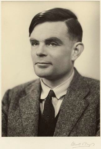 Historical black-and-white photo shows Alan Turing posing for a head shot.