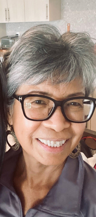 Nora, a Filipino woman, with short gray hair, black framed glasses, smiling.