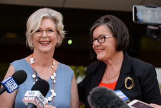 Independant MP Helen Haines stands to the left of Independant Cathy McGowan as they address the media. Microphones are pointed at them across the bottom of the image.