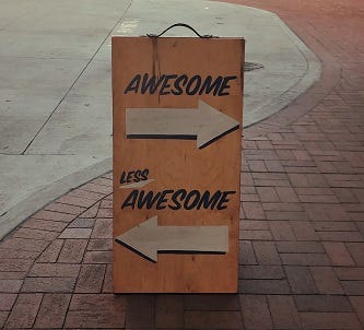 Sign on a pavement with the word “awesome” above an arrow pointing to the right, and the words “less awesome” above an arrow