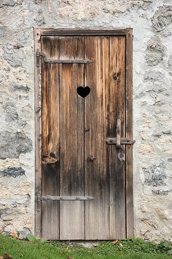 Uma foto da porta de um banheiro com um coração cortado na madeira