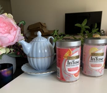 A teapot and two jars of tea are placed on a desk, next to flowers and candles.