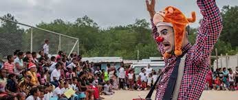 Clown interacting with a large group of children/adolescents outdoors.