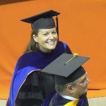 Standing in my cap and gown at my graduation with an organge banner in the background.