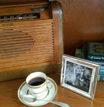 A cup of coffee sits next to an old-time radio on a shelf.