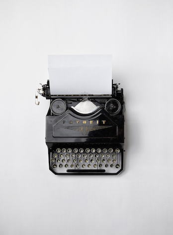 An antique typewriter with a blank piece of paper sits on a white desk