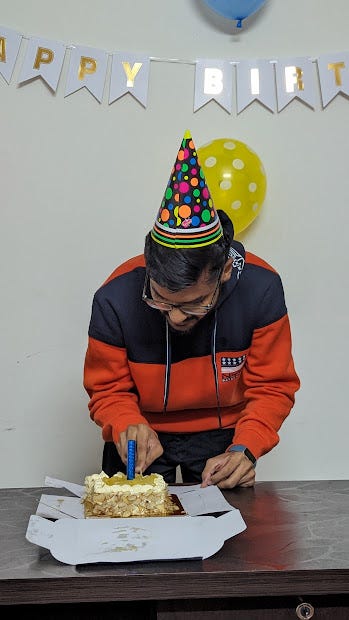 Me cutting a cake wearing a birthday hat and some decorations in the background