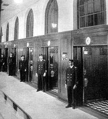 Male elevator operators are pictured outside of their respective elevators.