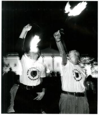 Duas participantes do lesbian avengers usando uma camisa branca do grupo e protestando engolindo fogo.