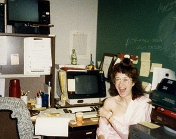 Bitsy as a young software engineer, circa 1984, with vending machine coffee and a pack of Lorna Doone cookies, goofing around in her office at IBM with a microfiche and a stuffed moose on her head.