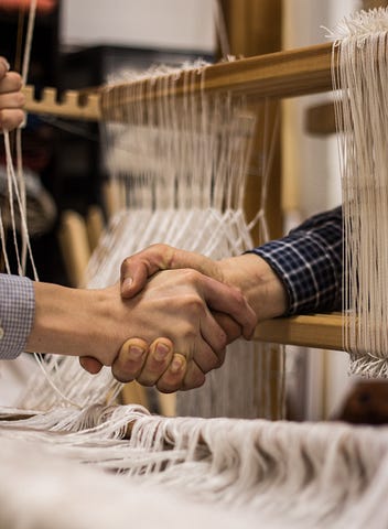 Photo of two people shaking hands — their bodies are not visible, and the handshake is happening through a loom.