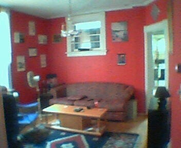 A photo of an interior living living room with a sofa, coffee table, and red painted walls. The photo is of very poor quality.