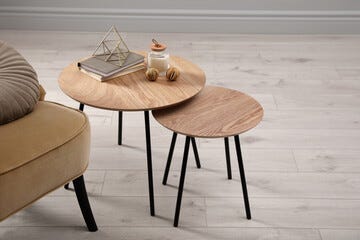 Wooden nesting tables with books and decor near armchair indoors