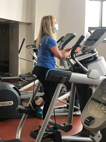 Woman in blue shirt and exercise close working out on elliptical machine.