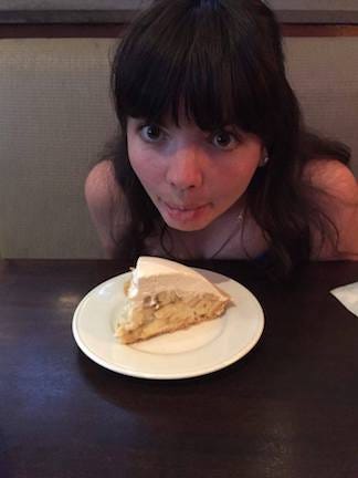 Anna leans head over banana cream pie on plate, sticking tongue out and making wide googly eyes at it.