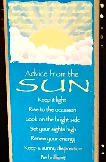 Color photo of a greeting card with sky-blue background, 3/4 yellow sun with rays streaming from a swath of white clouds atop, and below matching sun yellow writing amidst the blue stating line by line:” Advice from the, SUN, Keep it light, Rise to the occasion, Look on the bright side, Set your sights high, Renew your energy, Keep a sunny disposition, Be brilliant!”
