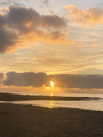 Sun rising into a bank of cloud over a calm sea, with a spit of black lava rock. Playa Honda, Lanzarote, 1st March 2023