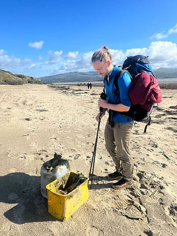 The author is carrying full gear and picking up trash on a beach with two containers in front of him.