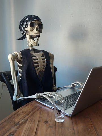 Plastic skeleton sitting by a computer and a shot glass