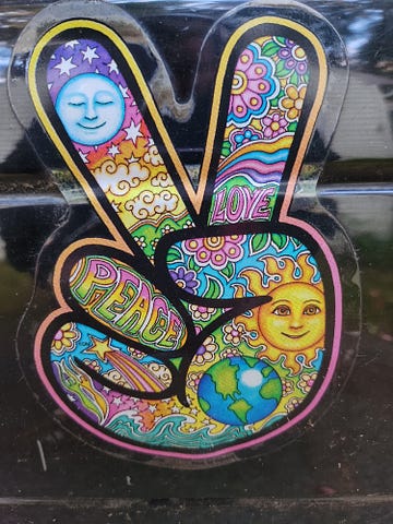 A peace symbol sticker of a hand showing the piece sign illustration. It has the sun and moon and colorful flowers and drawings inside it.