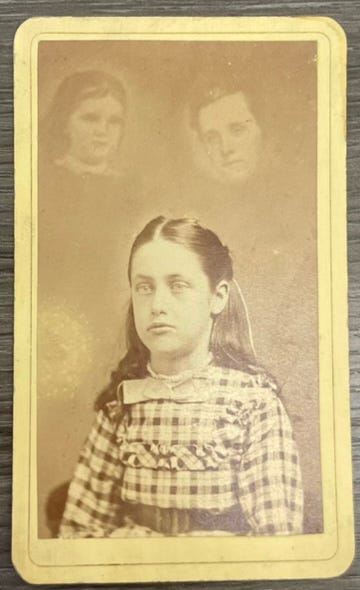 An old black-and-white photograph of a young girl. Two faces float behind her, looking like ghosts.
