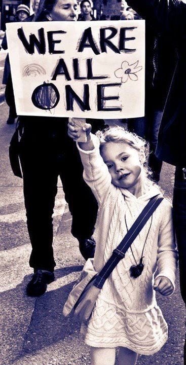 A young child standing with a sign that says “We are one.”