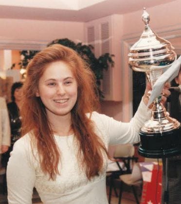 A young Judit Polgar celebrating her tournament victory by lifting up the trophy with a smile on her face.
