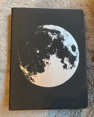 A black journal with the moon printed on the front in silvery-white.