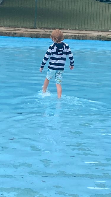 An image of Cheryl’s son wading through a paddling pool, with his back turned to the camera and moving away.