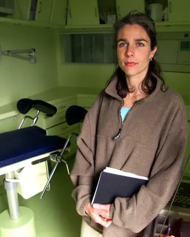 fotografia da Dra. Rebecca Gomperts em uma sala médica, ela esta trajada com um agasalho marrom, tem olhos azuis e cabelo médio castanho.