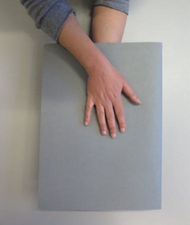 A conservator using hands on both outer sides of the archival grey cards to flip the flat item over, without the use of a folder.
