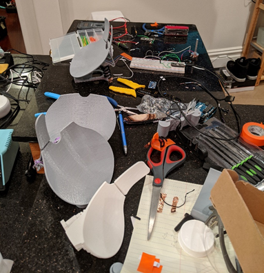 A messy kitchen table with many tools and 3D printed prototypes scattered across it.