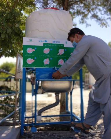 A man wearing a mask demonstrates how to use a foot-operated handwashing station.