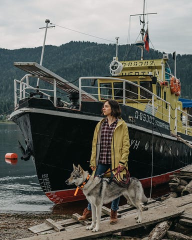 Image of a woman with dog on leash, in front of large fishing boat.
