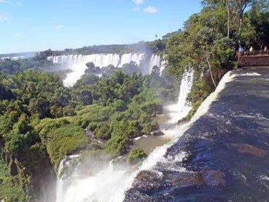 A view from the top of a waterfall at Iguazu Falls, overlooking a curved row of waterfalls falling down into lush rainforest