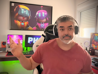 Charles, um homem branco com cabelos grisalhos está usando uma camiseta vermelha, um headset, sentado em uma cadeira gamer com quadros e telas ao fundo do jogo PK XD, em seu workstation.