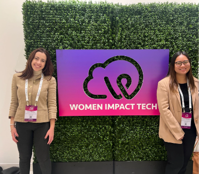 Alex and Camille smiling in front of a Women Impact Tech sign as they attend the conference in NYC.