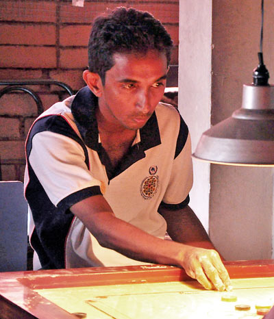 Nishantha Fernando sitting in front of the carrom board is about to make his move