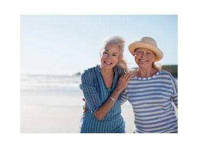 Two senior women posing for a vacation picture on a beach.