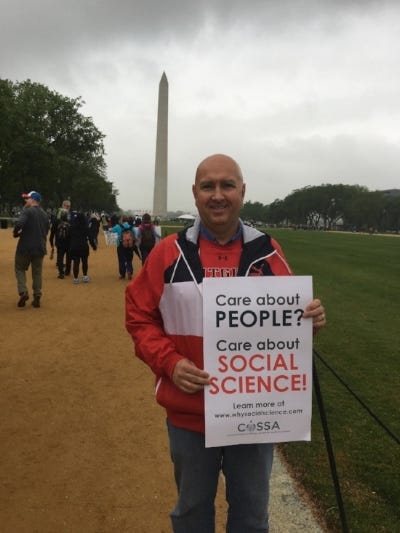 Craig Scott stands on the National Mall during the March for Science, holding a sign that reads 