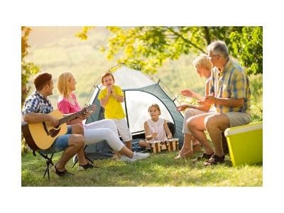 Family with three generations camping with man playing guitar