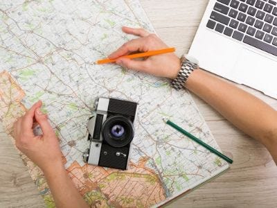 Image of map, camera, and laptop with hand holding pencil.