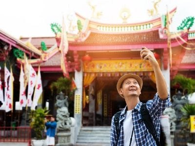 Senior man on vacation taking a selfie in front of a pagoda.