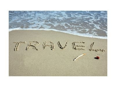 Surf with the word travel written in the wet sand.