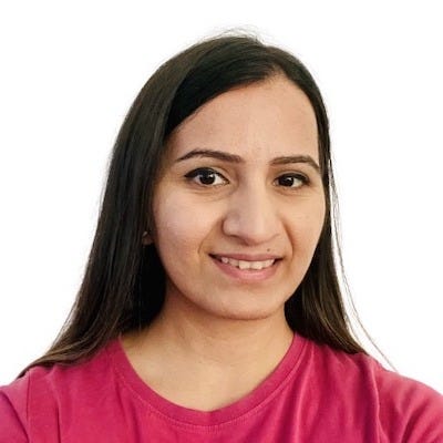 Photo of Harneet, an Asian woman, from the chest up. She is smiling at the camera. She is wearing a shade of pink. She has long black hair.