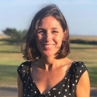 Sarah Beck looks at the camera and smiles for a portrait with a green field in the background.