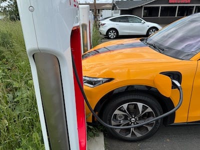 The nose of the car poking between two supercharger upright stations so the charging cable can reach