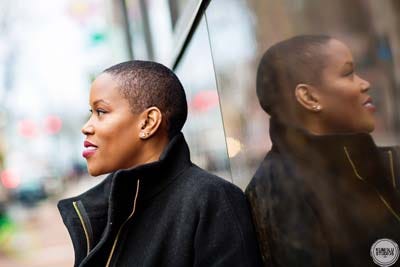 Meredith D. Clark looking left out a window, with her reflection in a glass building front to the right.